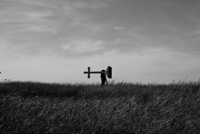 Person carrying cross on grassy field against sky