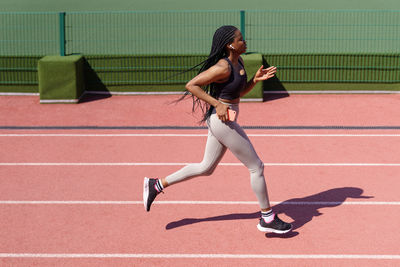 Young woman in headphones runs every day on red track at sports ground of big residential complex