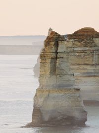 Rock formation by sea against clear sky
