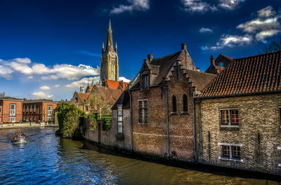 View of old building by canal against cloudy sky