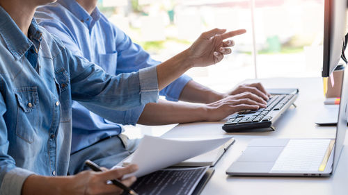 Midsection of computer programmers using computer on office desk