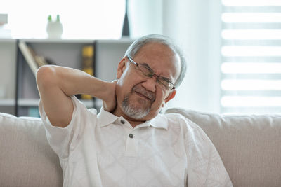 Close-up of mature man with neck pain sitting on sofa at home