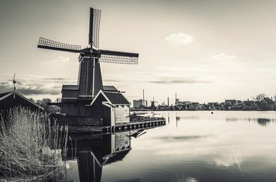 Traditional windmill by river against sky