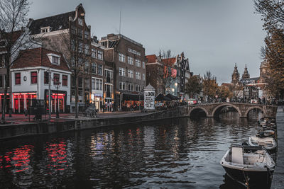 Bridge over canal by buildings against sky in city