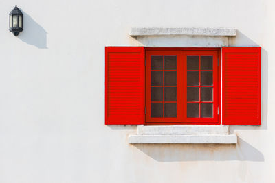 Colorful red window and detail of house exterior on white wall.