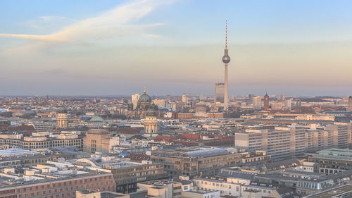 Fernsehturm amidst cityscape against sky during sunset