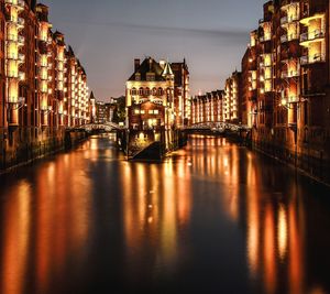 Bridge over river amidst buildings in city at night