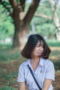Smiling young woman tossing hair while sitting at park