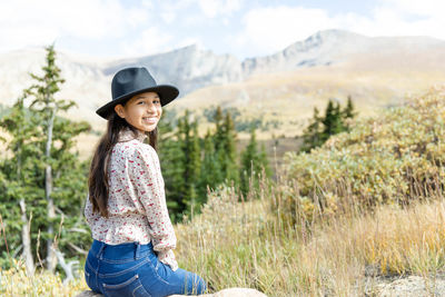 Portrait of hispanic young girl smiling at the camera while sitting in front of mountain scenery