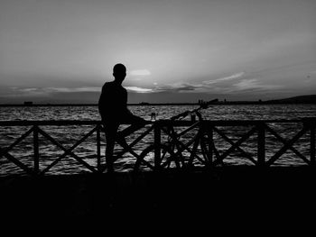 Silhouette man with bicycle on promenade with sea in background against sky