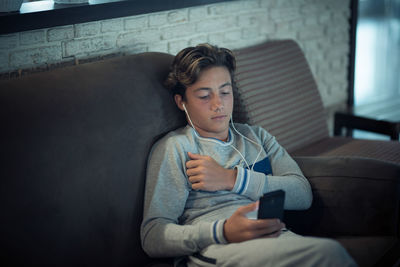 Teenage boy using smart phone while relaxing on sofa at home