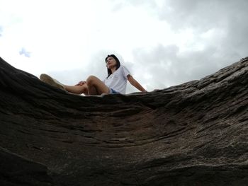 Low angle view of woman sitting on rock against sky