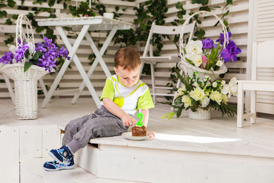 Full length of boy sitting by potted plant