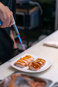 Cropped hand of person burning salmon sushi on table