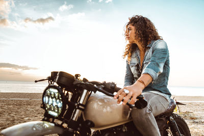 Woman riding motorcycle on beach against sky