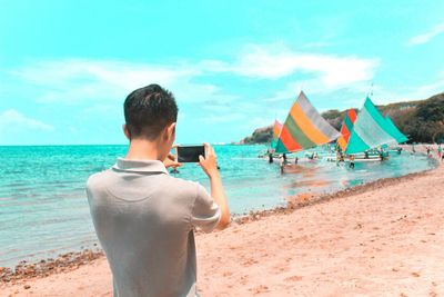 Rear view of man photographing nautical vessels at beach