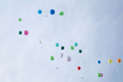 Low angle view of colorful helium balloons flying against sky