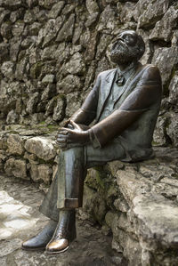 Low section of man sitting on rock against wall