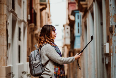 Side view of woman holding monopod standing in alley