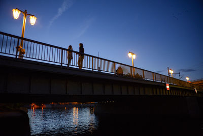 People on illuminated bridge against sky at dusk