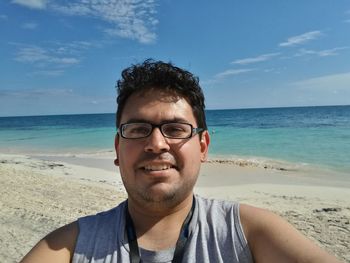 Close-up portrait of young man standing at beach against blue sky