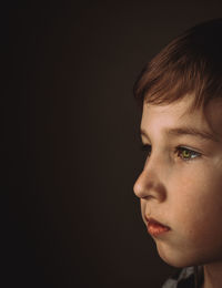 Close-up of boy looking away against black background