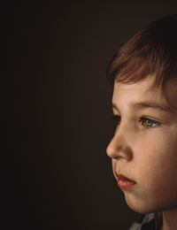 Close-up portrait of boy looking away against black background