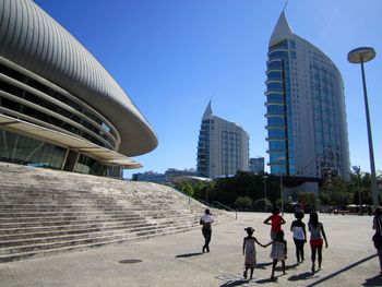 People walking by modern buildings against sky in city