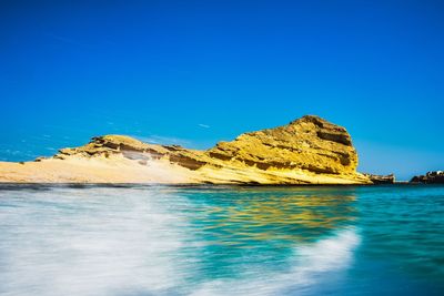 Scenic view of sea and rocks against clear blue sky