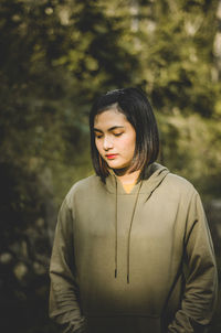 Young woman looking away while standing against trees