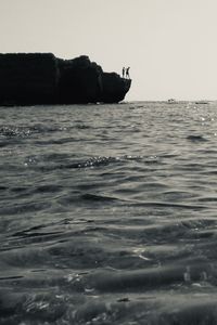 Silhouette rocks in sea against clear sky