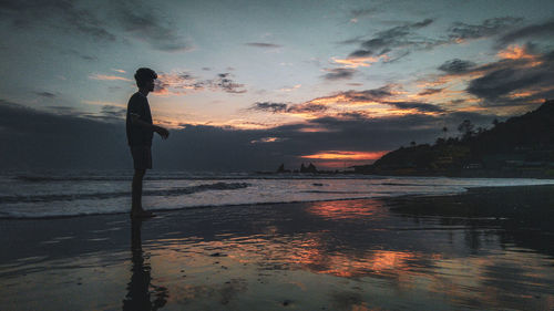 Silhouette man standing on beach against sky during sunset