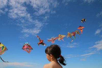 Low angle view of girl by kites flying in sky