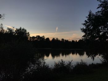 Silhouette trees by lake against sky during sunset
