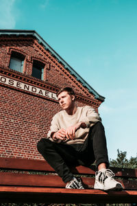 Low angle view of young man sitting against built structure