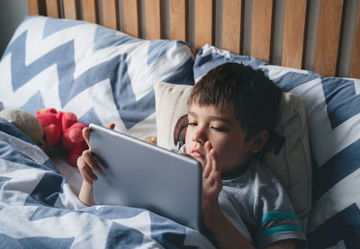 Rear view of boy using mobile phone on bed