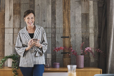 Portrait of happy businesswoman holding smart phone against wood paneling in portable office truck