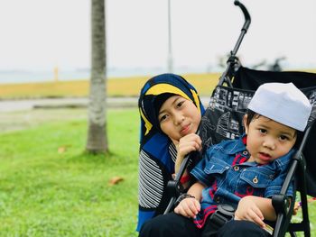 Portrait of sister with brother sitting on baby carriage at park