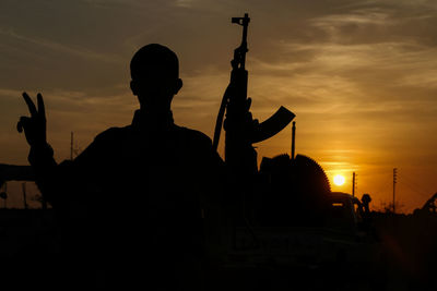 Silhouette soldier holding rifle standing against sky during sunset