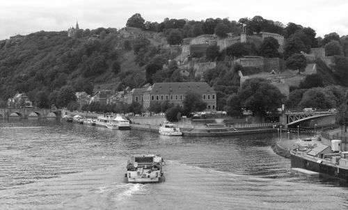 Boats sailing on river by trees against sky