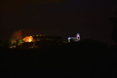 Silhouette man sitting in illuminated city against sky at night