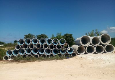 Stack of pipes on field against clear blue sky