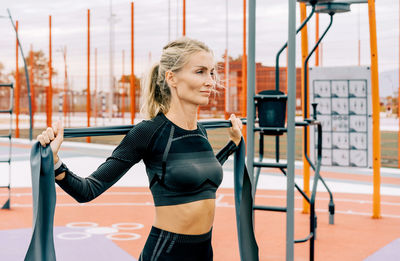 Young athletic woman is training on the sports ground using sports elastic bands.