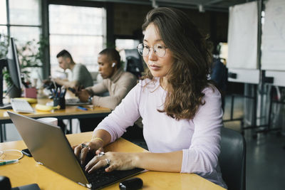 Female computer programmer coding on laptop at desk in startup company