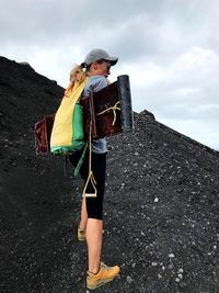 Woman carrying plank and backpack while climbing mountain against sky