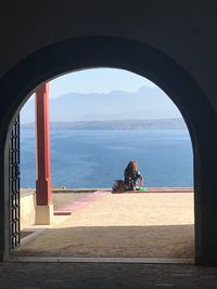 Rear view of man sitting at beach seen through window