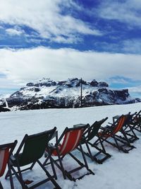 Chairs and snowcapped mountains against sky during winter