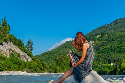 Young woman sitting on mountain against blue sky