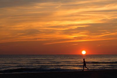 Silhouette man jogging on beach against orange sky