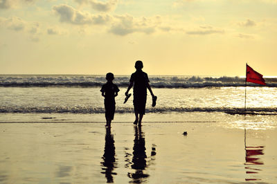 Rear view of siblings walking on shore at beach during sunset